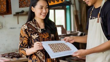 Ilustrasi seorang desainer yang mendesain motif batik, menyerahkan hasil desainnya untuk dikerjakan perajin batik.