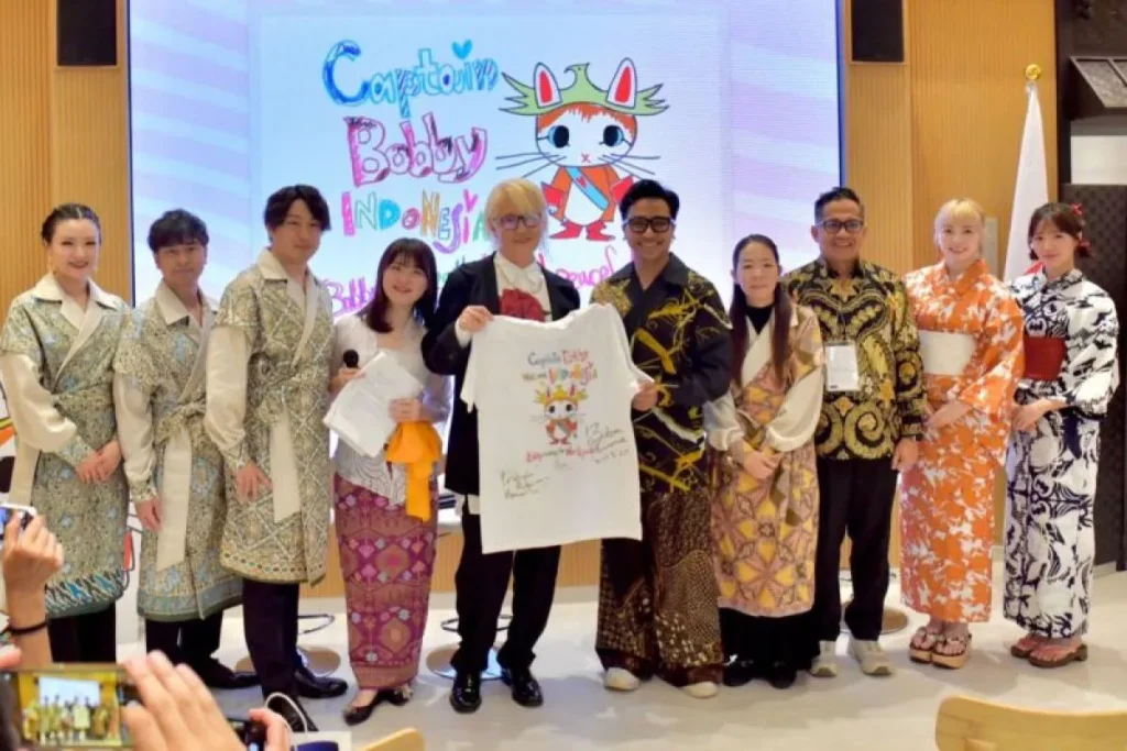 Direktur Kreatif Jember Fashion Carnival (JFC) sekaligus Penata Rias Bubah Alfian (kelima dari kanan) memberikan suvenir berupa kaus oblong bergambar kucing ikonik Presiden Prabowo Subianto, “Kapten Bobby,” kepada pelukis kontemporer Jepang Inoue Bunta (kelima dari kiri), didampingi para pendiri Yayasan Sakuranesia Sakura Ijuin (keempat dari kanan) dan Tovic Rustam (ketiga dari kanan), usai dialog budaya di Expo Osaka 2025, Paviliun Indonesia, Kansai, Jepang, Selasa (10 Juni 2025).
