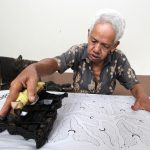 Seorang perajin batik Banyumas sedang membuat motif menggunakan cap di kain batik