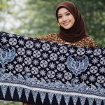 Buat gambar ukuran 1920 x 1080 piksel (landscape): Perempuan cantik Indonesia sedang membentangkan motif batik Kamis Legi