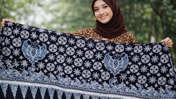 Buat gambar ukuran 1920 x 1080 piksel (landscape): Perempuan cantik Indonesia sedang membentangkan motif batik Kamis Legi