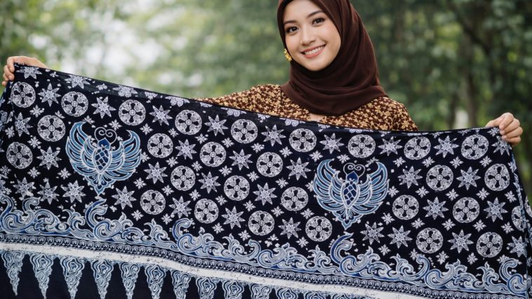 Buat gambar ukuran 1920 x 1080 piksel (landscape): Perempuan cantik Indonesia sedang membentangkan motif batik Kamis Legi