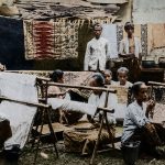 buat gambar foto ukuran 16:9. Konsep foto: Seorang gadis Indonesia menggunakan kain dodot ditutupi selendang warna kuning sedang merentangkan kain putih dengan motif batik belum jadi di gawangan. Masa itu era tahun 1930-an.